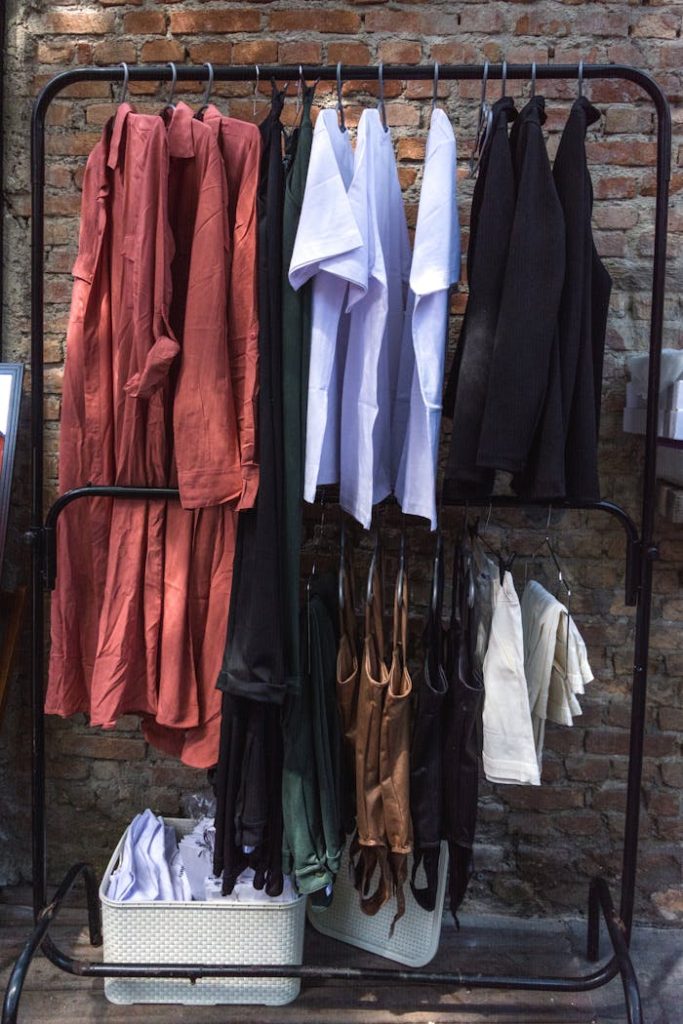 A diverse collection of garments neatly hung on a clothing rack against a rustic brick wall, showcasing fashion variety.
